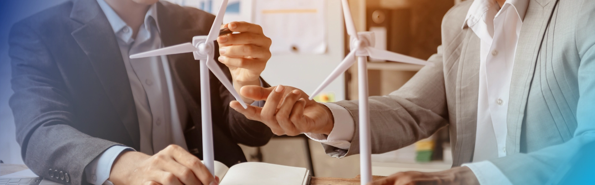 Two people, dressed in suits, discussing wind energy innovation with miniature turbine models in their hands.